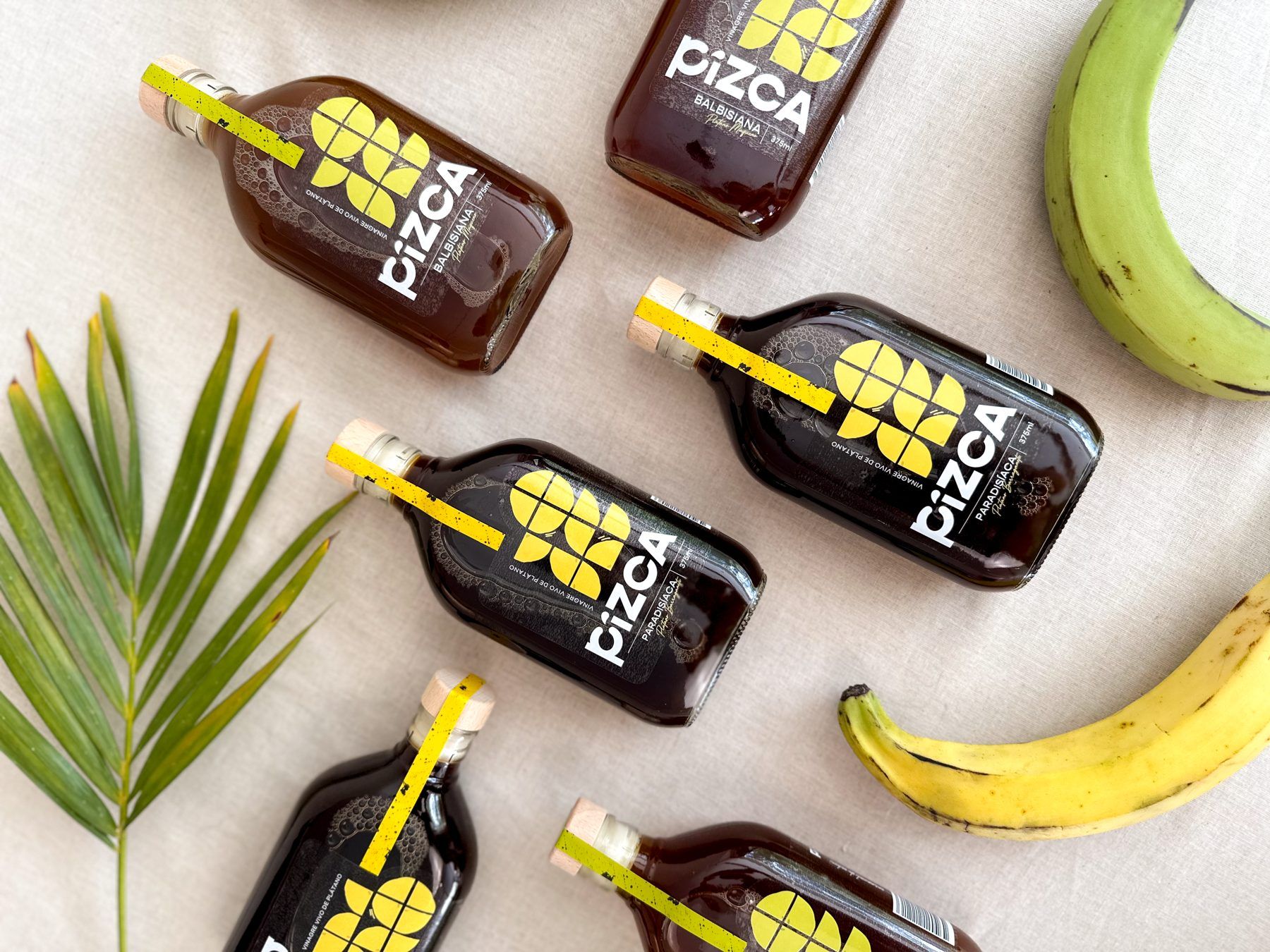 Botellas de Pizca entre plátanos verdes y maduros y hojas de palma