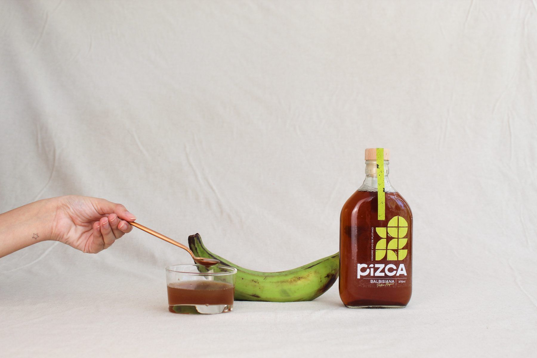 Cuchara sirviendo vinagre junto a un plátano verde